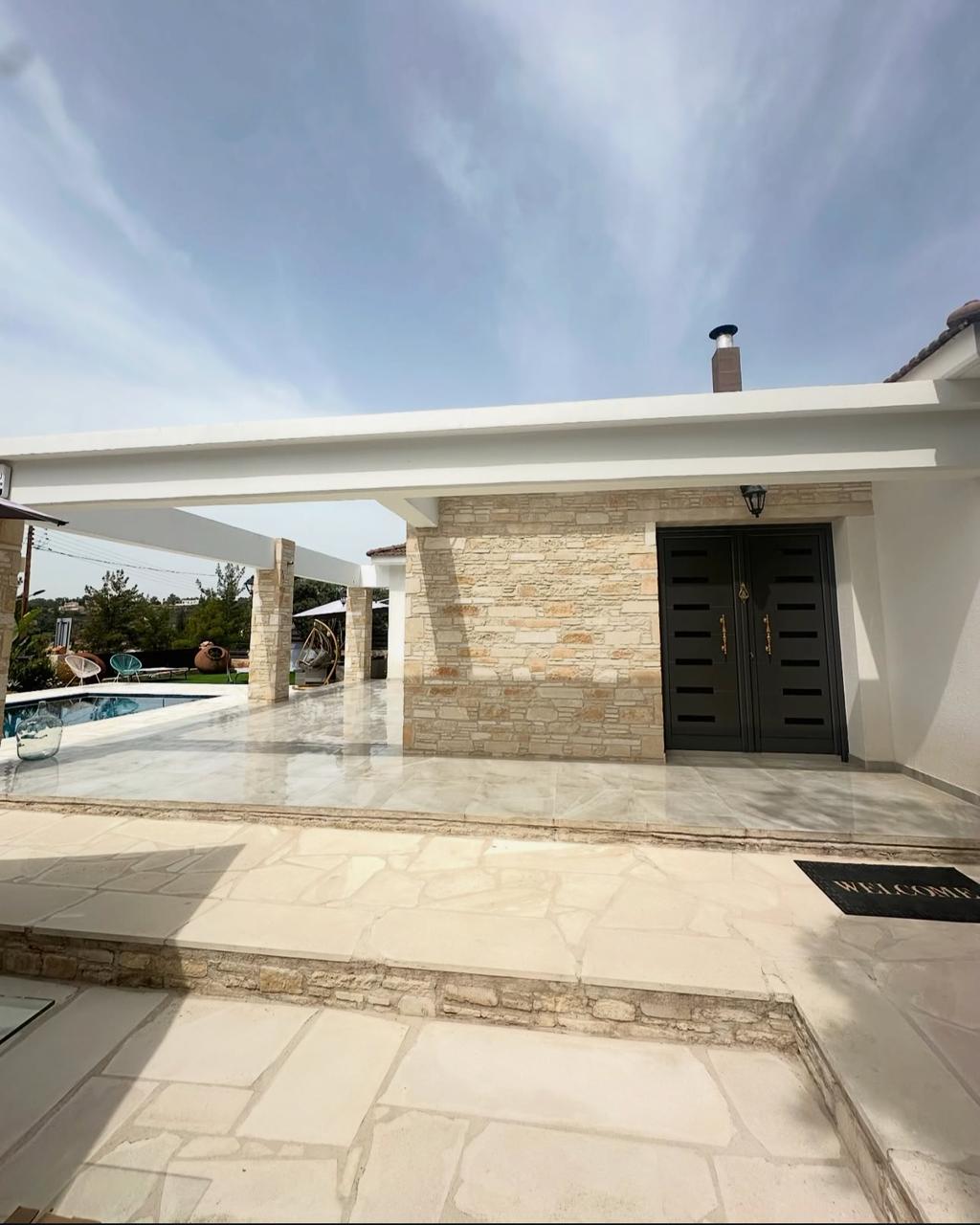 Bungalow entrance in Souni-Zanakia with dark double doors, stone pillar and marble courtyard