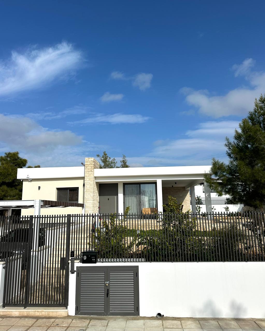 Modern flat-roof bungalow in Souni-Zanakia behind a gated fence with mature pines